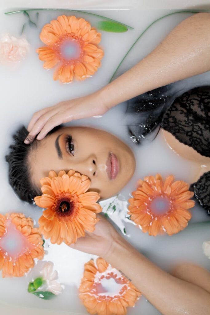 pexels-foto-3427769 Mujer con top de encaje negro relajándose en un baño de leche con flores naranjas.